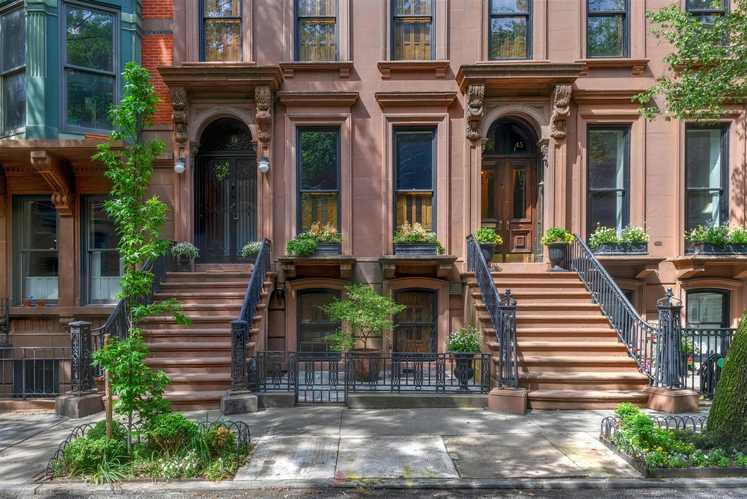 A row of brownstones with high stoops, iron railings and window boxes